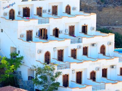 White terraced hotel building on a hillside with a wooded background.
