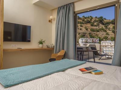 Helles Hotelzimmer mit Doppelbett, TV, Schreibtisch und Balkon mit Bergblick.