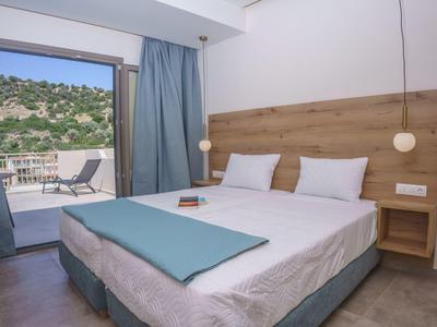 Modern eingerichtetes Hotelzimmer mit Doppelbett und Terrasse mit Blick auf grüne Hügel.