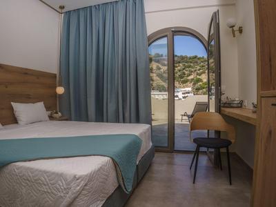 Schlichtes Hotelzimmer mit Bett, Schreibtisch und Balkon mit Blick auf Hügel.