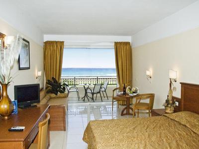 Pokój hotelowy z podwójnym łóżkiem, biurkiem, telewizorem i balkonem z widokiem na morze
