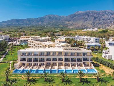 Nowoczesny kompleks hotelowy z prywatnymi basenami przy każdej apartamencie, otoczony zielonymi trawnikami i górami w tle.