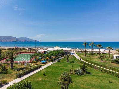 Widok na plażę z palmami, boiskiem sportowym i ścieżkami pod niebieskim niebem.