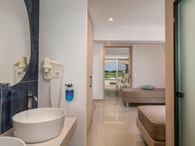 Moderner Hotelzimmergang mit rundem Spiegel, weißem Waschbecken und Blick zu Betten und Balkon.