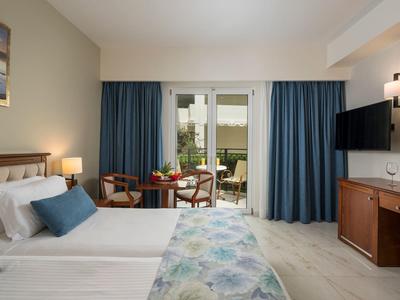 Modern eingerichtetes Hotelzimmer mit Doppelbett, Sitzbereich, Flachbildfernseher und Blick auf Terrasse.