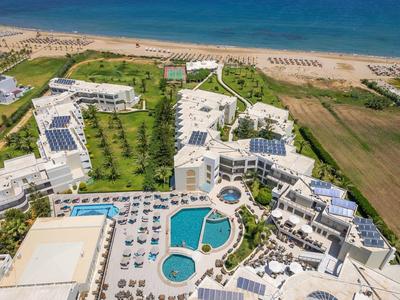Luftaufnahme eines Hotels mit mehreren Pools, Liegestühlen, Grünflächen und Strand im Hintergrund.