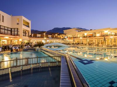 Oświetlony hotel z dużym basenem i mostem o zmierzchu w górskim otoczeniu.