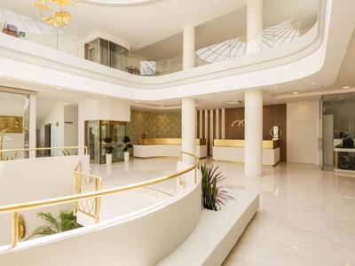 Przestronny, nowoczesny hol hotelowy z białymi ścianami, kolumnami i złotymi akcentami.