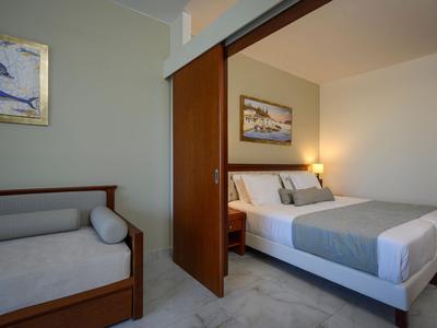Nowoczesny pokój hotelowy z podwójnym łóżkiem, leżanką i minimalistyczną dekoracją.