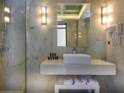 Nowoczesna łazienka hotelowa z umywalką, lustrem i prysznicem w jasnym marmurowym wyglądzie.
