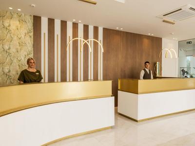 Nowoczesna recepcja hotelowa z dwoma pracownikami za kremowo-złotymi ladami.