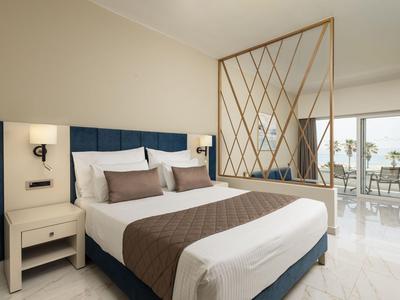 Nowoczesny pokój hotelowy z dużym łóżkiem, eleganckim parawanem i balkonem z widokiem na morze.