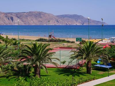 Zielony ogród z palmami przed piaszczystą plażą i morzem z górami w tle.