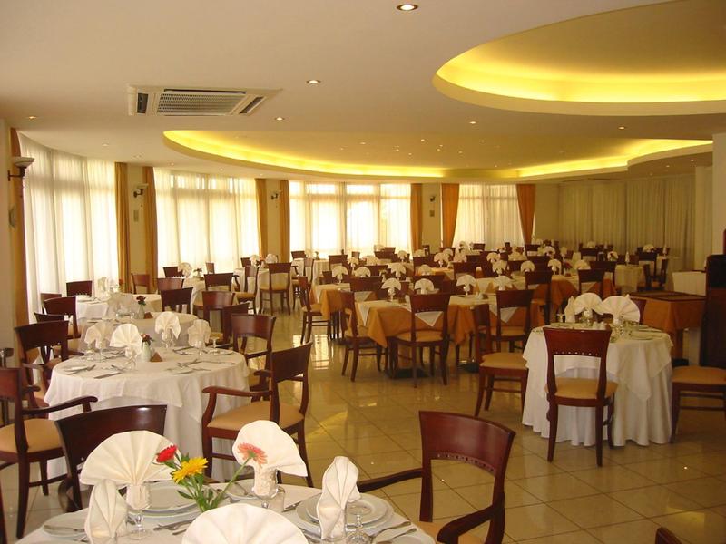 Großes Hotel mit mehreren Pools, grünen Rasenflächen und Bergen im Hintergrund unter blauem Himmel.