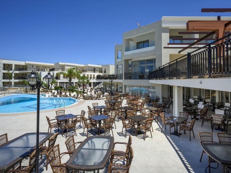 Große Terrasse mit vielen Stühlen und Tischen am Pool eines modernen Hotels bei klarem Himmel.