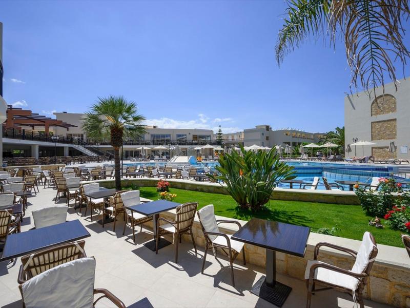 Außenpool mit Liegestühlen, Gräsern und Tischen im sonnigen Hotelgarten mit blauem Himmel.