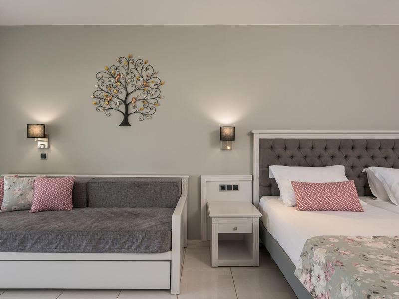 Modernes Hotelzimmer mit Bett, Couch, Nachttisch und dekorativem Baum an der Wand.