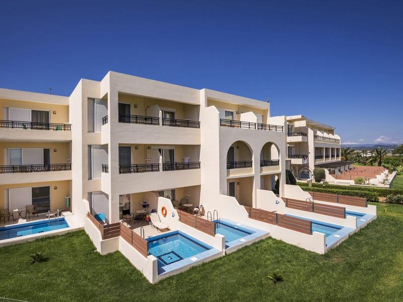 Modernes, weißes Appartementhaus mit Balkonen, Pools und gepflegtem Rasen unter klarem blauen Himmel.