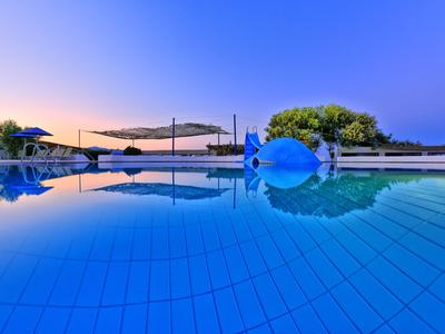 Una piscina tranquilla con ombrelloni e alberi sullo sfondo sotto un cielo sereno al tramonto.