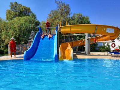 Děti sjíždějí modrou a žlutou vodní skluzavkou do bazénu.