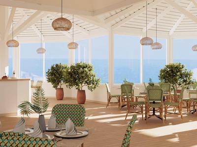 Světlá, vzdušná jídelna s výhledem na moře, stoly a zelené rostliny.