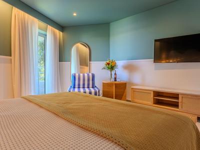 Gemütliches Hotelzimmer mit Bett, Stuhl, Blumen und Fernseher an der Wand.