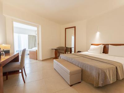Helles Hotelzimmer mit großem Bett, Schreibbereich und Sitzgelegenheiten.