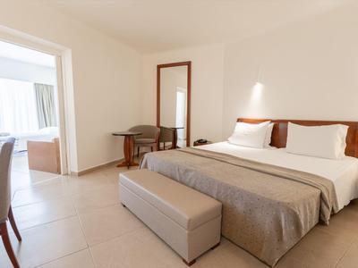 Helles Hotelzimmer mit großem Bett, Tisch, Stühlen und Zugang zu einem Badezimmer.
