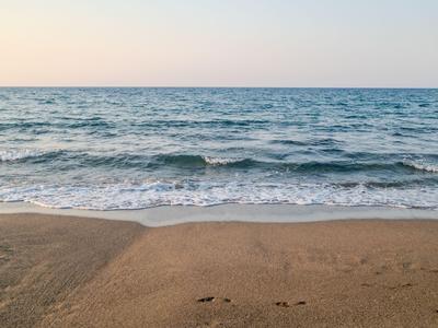 Sandstrand mit sanften Wellen und klarem Himmel im Hintergrund.