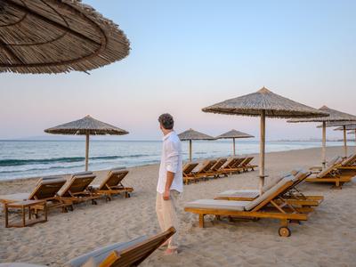 Mann steht am Strand neben leeren Liegestühlen und Sonnenschirmen bei Sonnenuntergang.