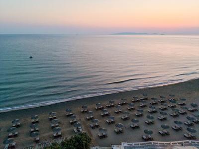 Sandstrand mit Reihen von Sonnenschirmen und ruhigem Meer bei Sonnenuntergang.