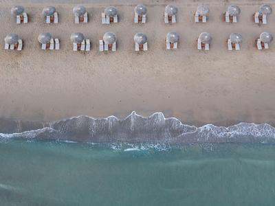 Vogelperspektive auf Reihen von Strandkörben am Sandstrand mit Wellen am Wasser.