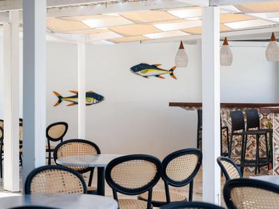 Heller Hotelbarbereich mit schwarzen und rattanfarbenen Stühlen und maritimen Dekorationen an der Wand.