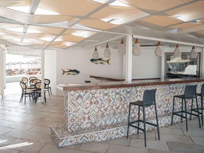 Helle Hotelbar mit gemustertem Mosaik, schwarzen Barhockern und Tisch mit Stühlen im Hintergrund.