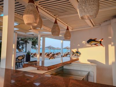 Helle Lounge mit Holzmöbeln, exotischen Lampen und Poolblick bei Sonnenuntergang.