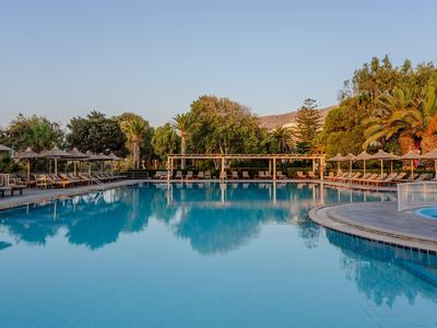 Großer Hotelpool mit klar blauem Wasser, umgeben von Palmen und Liegestühlen bei sonnigem Wetter.