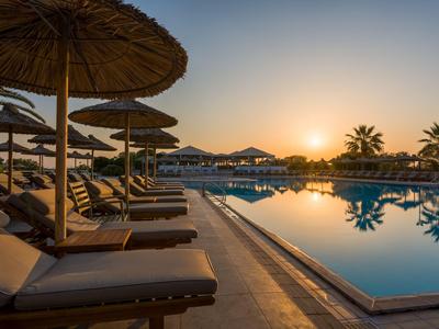 Sonnenuntergang über einem Pool mit Liegestühlen und Sonnenschirmen in einem Hotelresort.