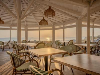 Helles, luftiges Restaurant mit Korbstühlen und Holzdecken, Blick auf Sonnenuntergang am Meer.