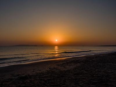 Sonnenuntergang über ruhigem Meer mit Strand im Vordergrund.