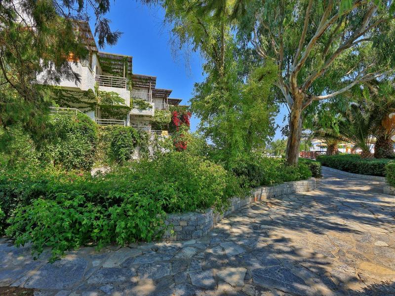 Hotel s balkony obklopený stromy a dlážděnou cestou v popředí