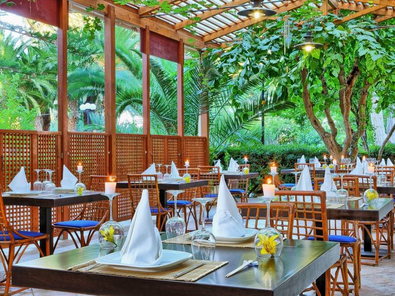 Pohodlná venkovní restaurace s prostřenými stoly a bohatou zelení.