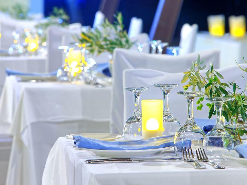 Elegantně prostřený stůl v světlé restauraci s bílými stoly a svíčkami.