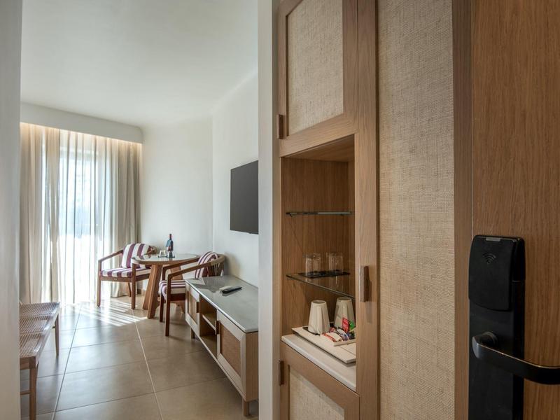 Moderní hotelový pokoj s dřevěným nábytkem, psacím stolem a závěsy na velkých oknech.