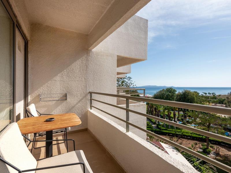 Balkon s výhledem na moře, dvě židle a malý stůl za slunečného počasí.