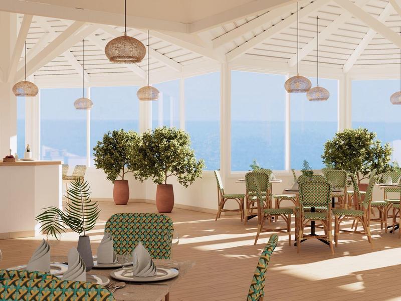 Světlá, vzdušná jídelna s výhledem na moře, stoly a zelené rostliny.
