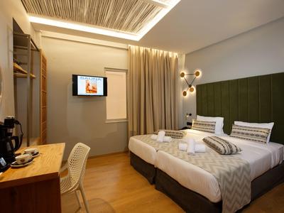 Modern hotel room with double bed, desk, TV, and warm lighting accents.
