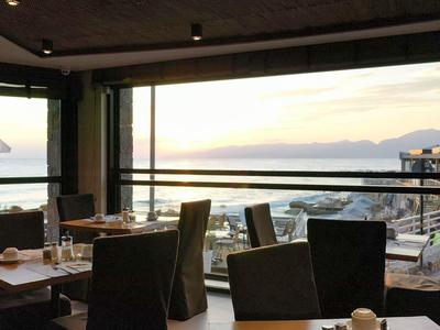 Ristorante moderno con posti a sedere vicino alla finestra e vista sul mare al tramonto.