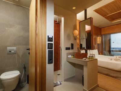Modern hotel bathroom with toilet, vanity, and view into bedroom with sea view.