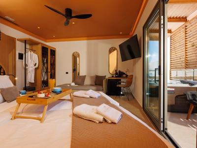 Cozy hotel room with bed, wooden table, TV, and balcony with outdoor seating.