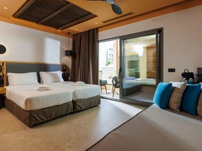 Modern hotel room with twin beds, lounge area, and large glass door to patio.
